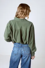 Camisa verde militar de manga larga con cuello camisero, cierre frontal con botones, dos bolsillos con solapa en el pecho y puños abotonados.