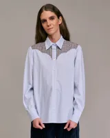 Camisa de manga larga con cuello abotonado, de corte recto, con canesú y puños a cuadros. El cuerpo de la camisa es a rayas verticales celestes y blancas.