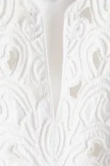 Blusa blanca de algodón con escote en V y pechera con broderie tono sobre tono embellecido con minicuentas y ribetes con pompones. Modelo de corte holgado con hombros caídos y mangas largas con tapeta de manga y puños abotonados. Bajo redondeado.