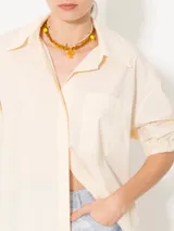 Camisa color crema de poplin liso, con acceso frontal a través de cartera oculta con seis botones forrados en tela base y un botón petra en el pie de cuello. Las mangas cortas finalizan en puño con elástico. Incluye un bolsillo plaqué con atraques triangulares para refuerzo y bordado marcario JCH en el lateral inferior.