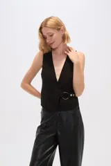 Chaleco negro sin mangas con escote en V y cierre cruzado con hebilla metálica.