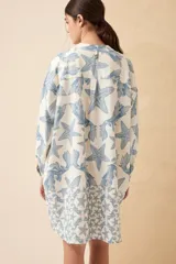 Vestido camisero corto de lino color blanco con estampado de estrellas de mar y algas en azul. Tiene cuello mao, mangas largas y cierre frontal con botones.