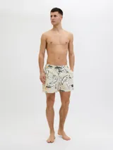 Short de baño color crema con estampado de flores y hojas en blanco, negro y amarillo. Tiene cintura elástica con cordón ajustable, bolsillos laterales y un bolsillo trasero.