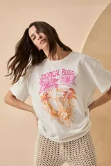Remera blanca de algodón con estampado de un tucán, palmeras y la frase 'Tropical Bliss' en tonos naranja y rosa.