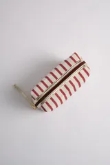 Neceser rectangular de tela color crudo con rayas verticales rojas. Tiene cierre superior con cremallera dorada y tira de mano lateral.
