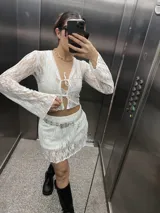 Top blanco de encaje elastizado con mangas largas y cierre frontal con lazo.