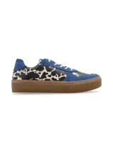 Zapatillas bajas con estampado de vaca en blanco y negro, detalles en gamuza azul y suela marrón.