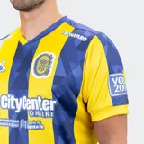 Camiseta de fútbol Le Coq Sportif del Rosario Central, modelo titular temporada 25/26. Diseño a rayas verticales amarillas y azules, con un patrón geométrico sutil en las franjas azules. Presenta cuello en V y detalles en azul en mangas y hombros.