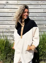 Buzo tipo poncho de polar color crudo con bloque superior en negro y detalles en beige.