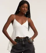 Blusa corta blanca de poliéster y elastano, con textura arrugada, escote en V, breteles finos y bajo asimétrico con volados laterales.