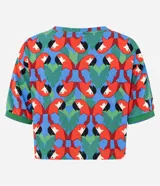 Remera de manga corta con cuello redondo y estampado repetitivo de loros rojos y hojas verdes sobre fondo azul y rojo. El borde de las mangas y el cuello es de punto acanalado verde.