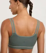 Top deportivo negro, corte tipo bralette, con escote asimétrico y doble tirante en los hombros. Presenta una banda elástica inferior con una delgada línea blanca horizontal.