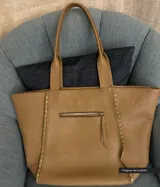 Bolso tipo tote de cuero color beige con textura granulada y tachas plateadas en los laterales.