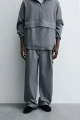 Pantalón cargo gris con textura acanalada, corte relaxed fit, cintura elástica con pliegues frontales, bolsillos laterales tipo cargo con solapa, bolsillos frontales y traseros de vivo, cierre frontal con cremallera y botón.