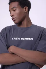 Camiseta de manga corta, color gris oscuro con efecto lavado, corte oversize y cuello redondo. Presenta texto estampado en blanco en el pecho que dice "CREW MEMBER".