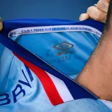 Camiseta de fútbol Umbro del Club Nacional de Football, modelo Away 3. Diseño celeste con detalles en azul y rojo en cuello y mangas. Incluye logo de Umbro, escudo del club y sponsors.