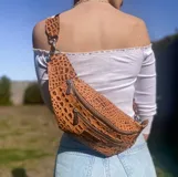 Riñonera de cuero color marrón con diseño de cocodrilo, tres compartimentos con cierre y correa ajustable.