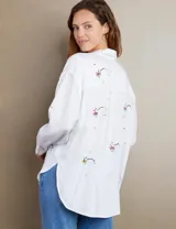 Camisa blanca con bordados coloridos y corte relajado, con botones frontales y dos bolsillos en el pecho.