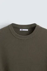 Jersey color crudo tejido en hilatura de algodón, con cuello redondo, manga larga y acabados en rib.