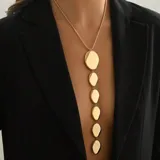 Collar largo dorado con cadena fina y dijes colgantes de formas geométricas irregulares.