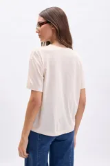 Remera color crudo de manga corta con cuello redondo y estampa marrón con la frase "Le Marais, Rue des Rosiers, France".