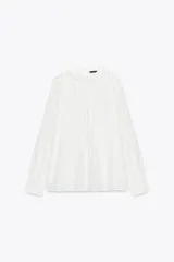 Blusa blanca de cuello redondo y manga larga con puños. Presenta bordados florales y entredoses combinados en el frente. Cierre en la espalda con abertura y botón.
