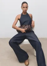 Mono largo de denim azul oscuro, sin mangas, con cuello halter y escote en la espalda. Presenta un corte recto y holgado en las piernas.