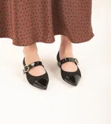 Zapato guillermina de gamuza negra con puntera de charol brillante y tira sobre el empeine con hebilla dorada. Tacón bajo y cuadrado.