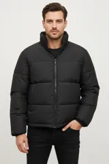 Campera acolchada negra, estilo puffer, con cuello alto y cierre frontal.