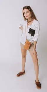 Camisa color naranja de lino o algodón con cuello clásico, cierre frontal con botones y mangas largas con puños abotonados. Presenta un bolsillo de cuero marrón en el pecho.