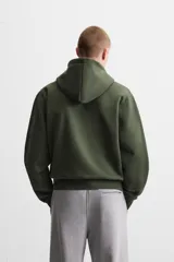 Sudadera negra relaxed fit de algodón compacto con interior en rizo, cuello con capucha ajustable, manga larga, bolsillos frontales tipo canguro, acabados en rib y cierre frontal con cremallera.