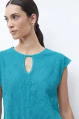 Remera verde petróleo con cuello redondo y abertura en forma de lágrima en el escote. Presenta un estampado geométrico en relieve y mangas cortas.