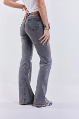 Pantalón de jean gris lavado, de tiro medio, corte ajustado en la cadera y acampanado desde la rodilla, con ruedo desflecado.