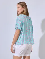 Blusa de gasa estampada color azul con puntos rosas, cuello redondo y escote en V, con mangas cortas y volados.
