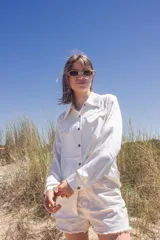 Camisa blanca de manga larga con cuello clásico y cierre frontal con botones. Tiene bolsillos con solapa en el pecho.