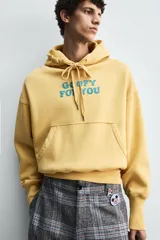 Sudadera con capucha color ocre, de corte holgado y mangas largas. Estampado frontal con texto en azul.