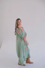 Vestido largo verde con estampado floral en tonos rosados y blancos, mangas 3/4 con ajuste de botón y ruedo irregular.