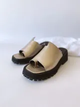 Sandalias doradas con tira para el dedo y suela track negra.