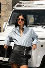 Minifalda negra de cuero con costuras horizontales y tres hebillas metálicas plateadas en el lateral.