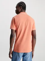 Chomba color salmón de corte slim fit, con cuello clásico y tapeta de dos botones. Presenta ribetes blancos en cuello y mangas, y logo CK bordado en blanco en el pecho.