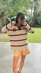 Buzo tipo rugby de algodón color beige con franjas horizontales negras y rosadas. Tiene cuello tipo polo con cartera negra y logo bordado en el pecho.