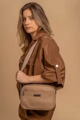 Bandolera color beige con textura de cuero granulado, con tres cierres principales, un cierre delantero y un bolsillo trasero. Incluye correa ajustable de tela en color beige claro.