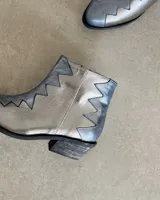 Botín de cuero vacuno color bronce con puntera y caña en cuero negro. Diseño con borde superior en zigzag y taco de madera.