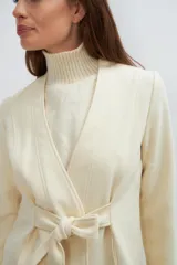 Chaqueta corta color beige, entallada, con escote en V, manga larga y cierre frontal con lazo fijo. Confeccionada en lana fina sin teñir, con bolsillos escondidos y terminaciones enviadas. Hecha 100% en Uruguay.