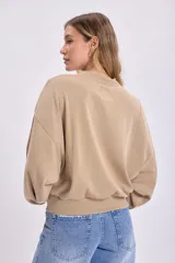 Buzo color beige de corte holgado, con cuello redondo y mangas abullonadas.