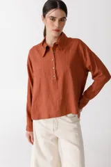 Blusa color ladrillo con rayas verticales finas, cuello tipo polo, manga larga y cierre parcial con botones.