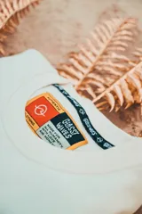 Buzo de tejido de punto color crudo con estampado frontal que incluye el texto "GLASSY WAVES" y un diseño de tabla de surf con alas.