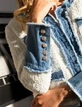 Chaqueta Nanette en tejido tweed color blanco y denim azul. Tiene cuello a la base, abertura central, bolsillos delanteros, puños con aplique de botones perlados, terminación desflecada y forro interno.