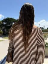 Vestido corto tejido a rayas horizontales marrones y blancas, con escote en V y mangas anchas.