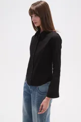 Camisa blanca de algodón, entallada, con cuello camisa y cierre frontal de botones. Presenta mangas largas con puños sencillos.